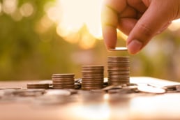 A hand stacks coins on a table outside.