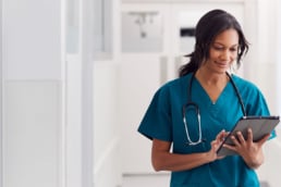 A nurse on a tablet in a white hallway