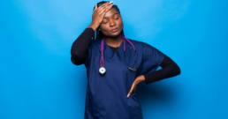 Nurse stands in front of a blue background with hand on her head showing how nurse mental health can suffer because of the job