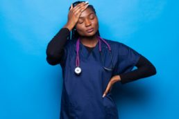 Nurse stands in front of a blue background with hand on her head showing how nurse mental health can suffer because of the job